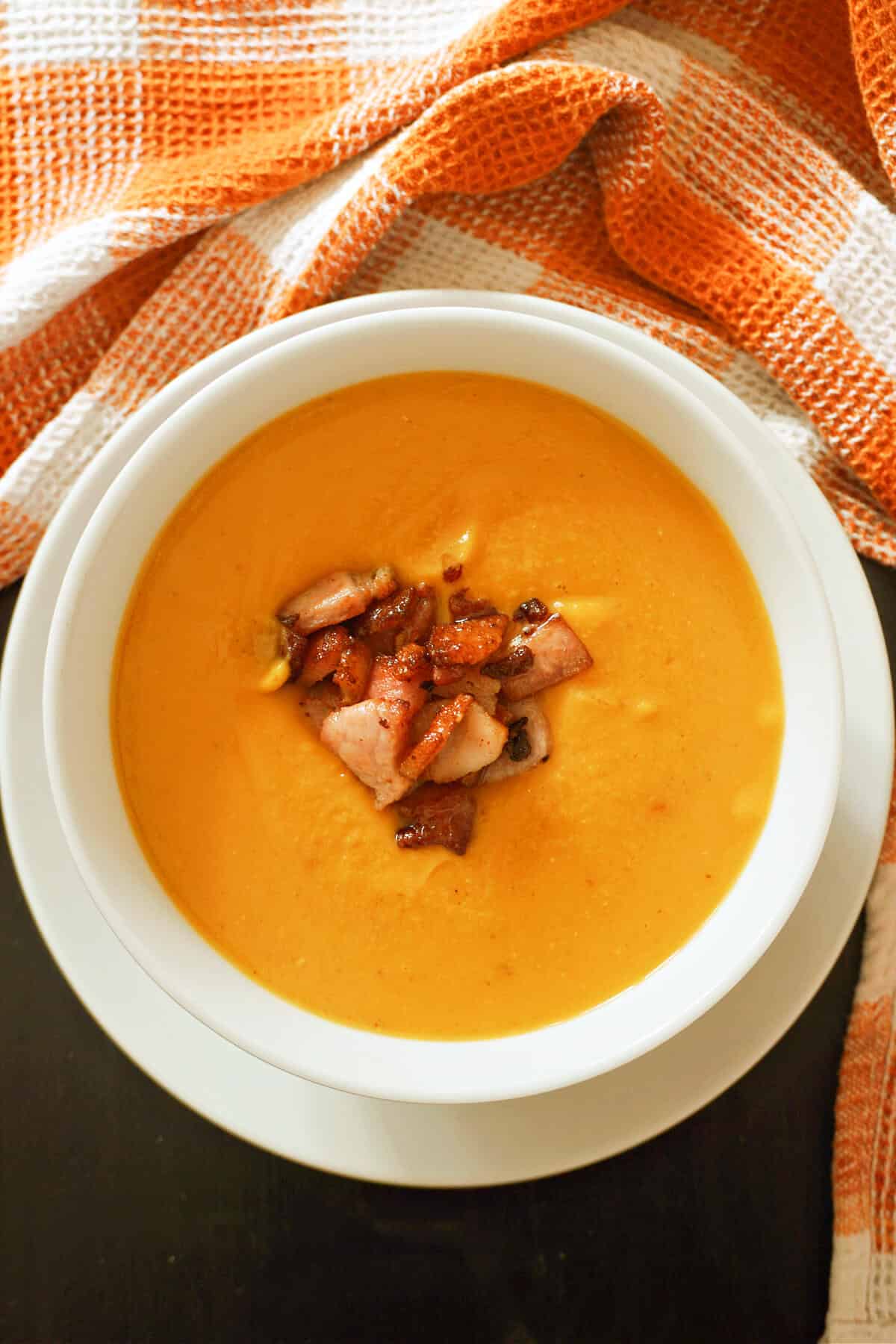 A white bowl with pumpkin soup topped with bacon pieces.