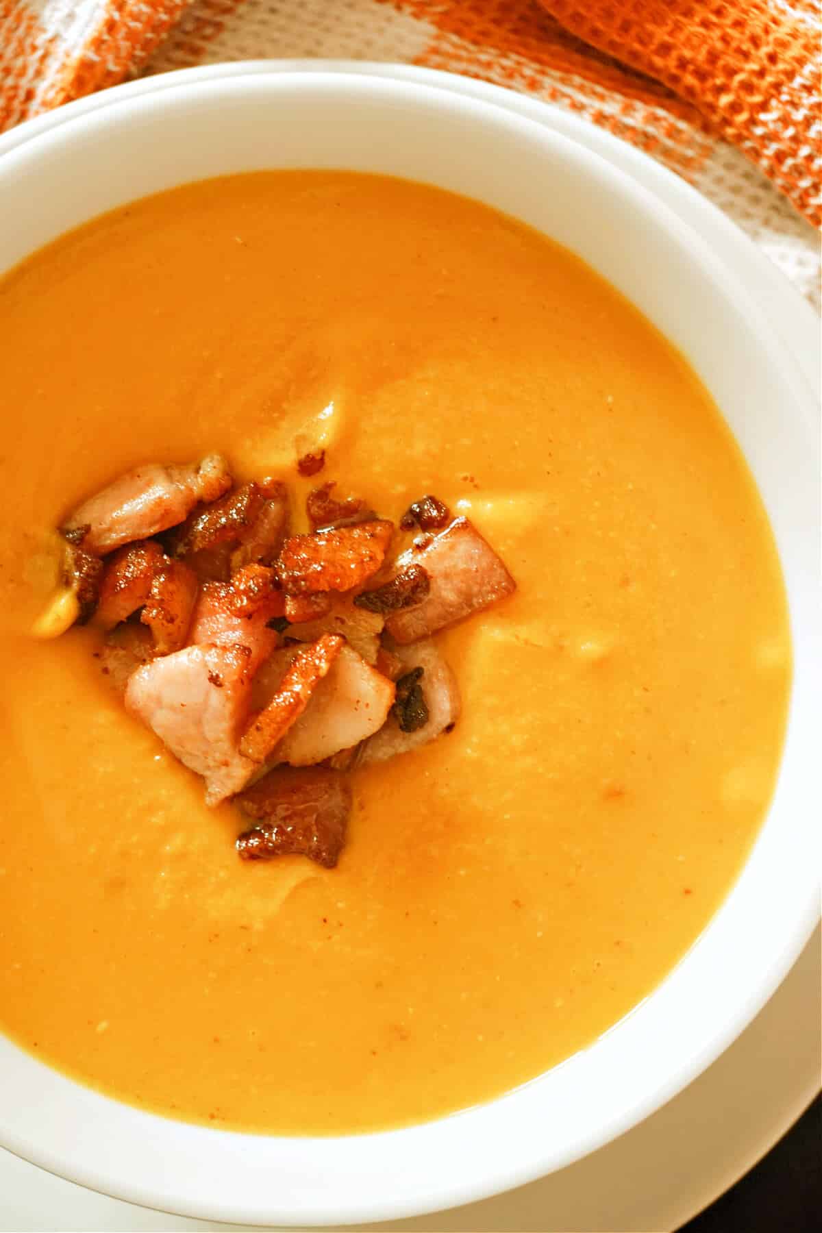 A white bowl with pumpkin and bacon soup.