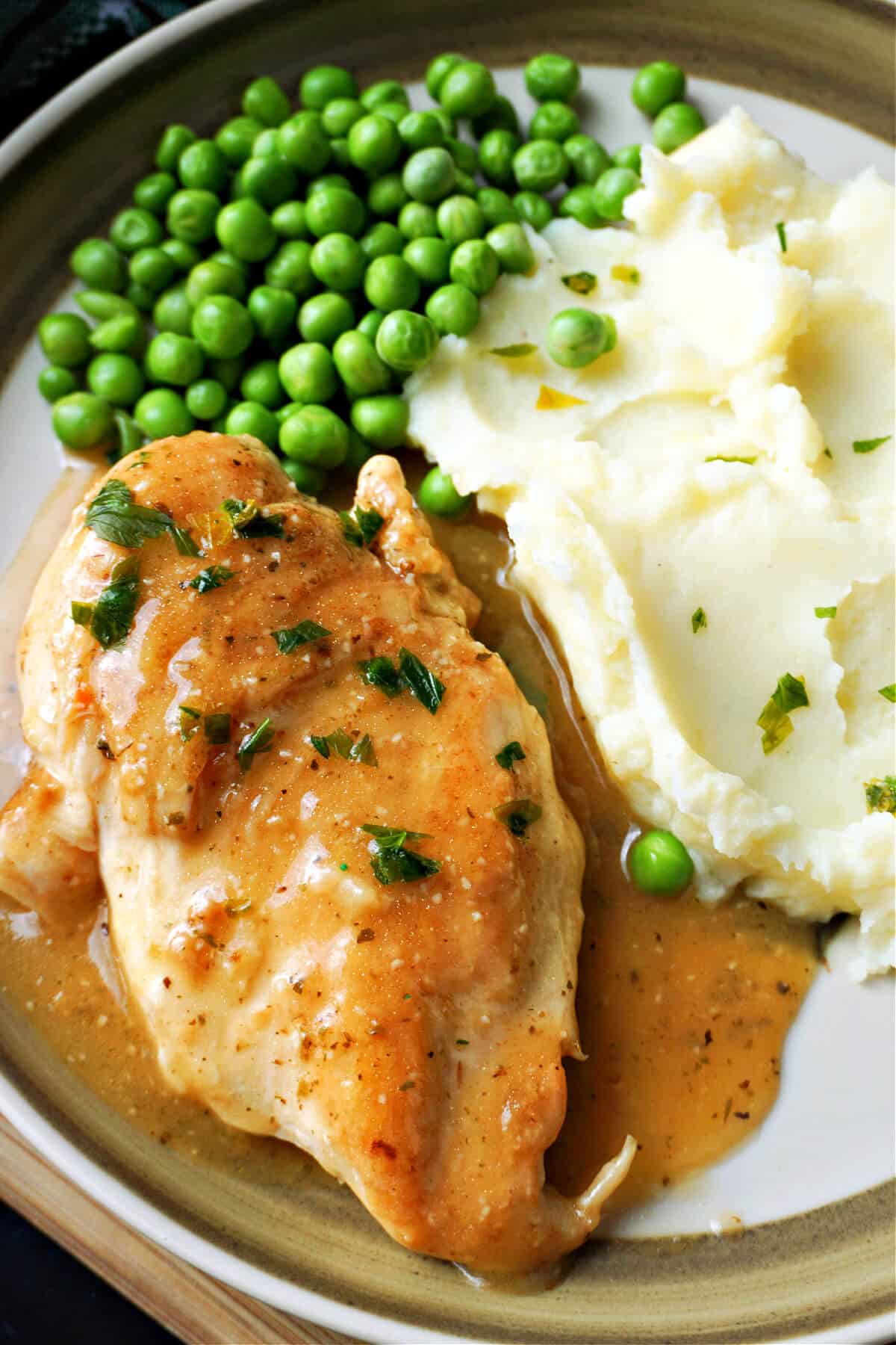 A plate with a chicken breasts smothered in gravy with mash and peas.