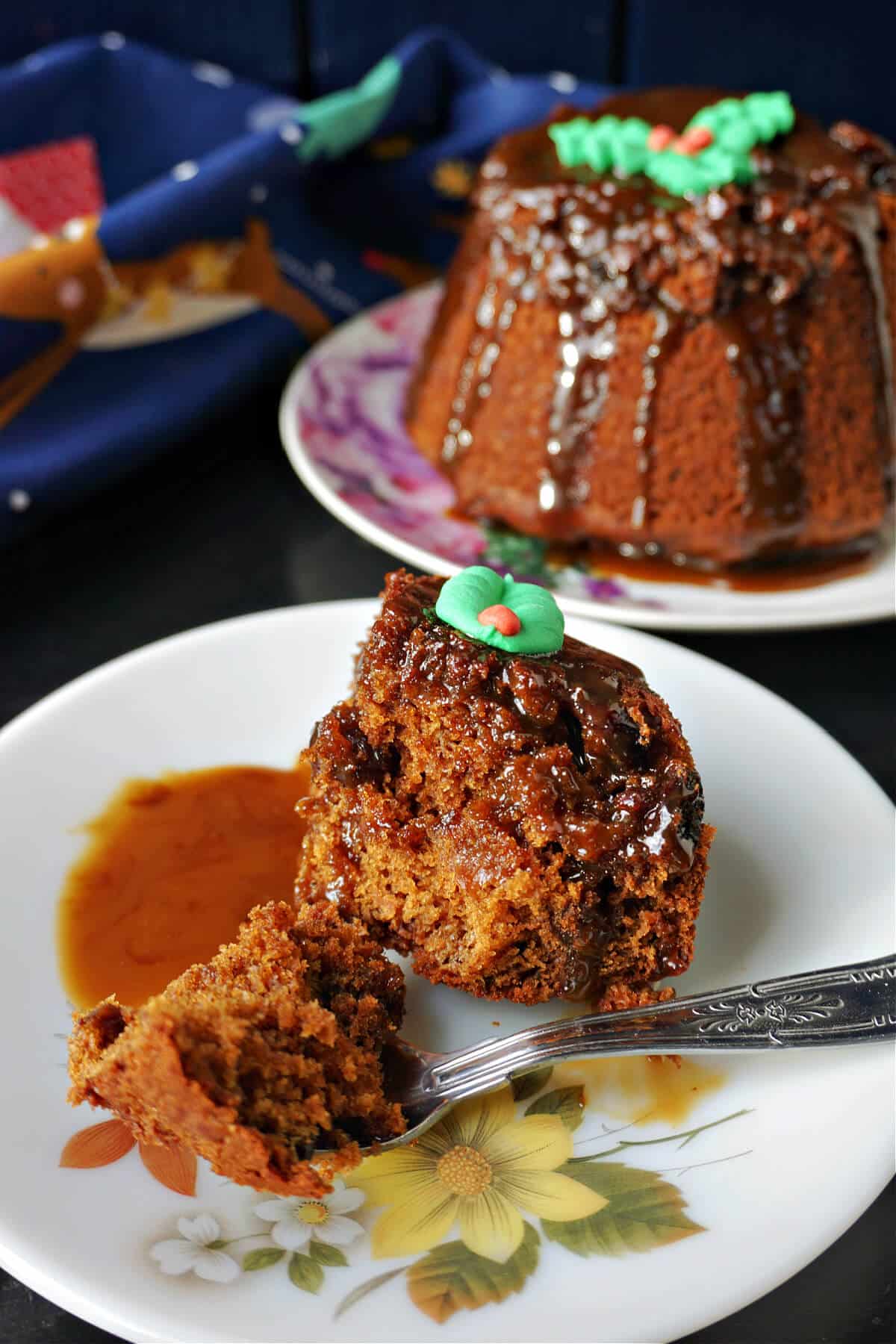 A portion of sticky toffee pudding with more Christmas pudding in the background.