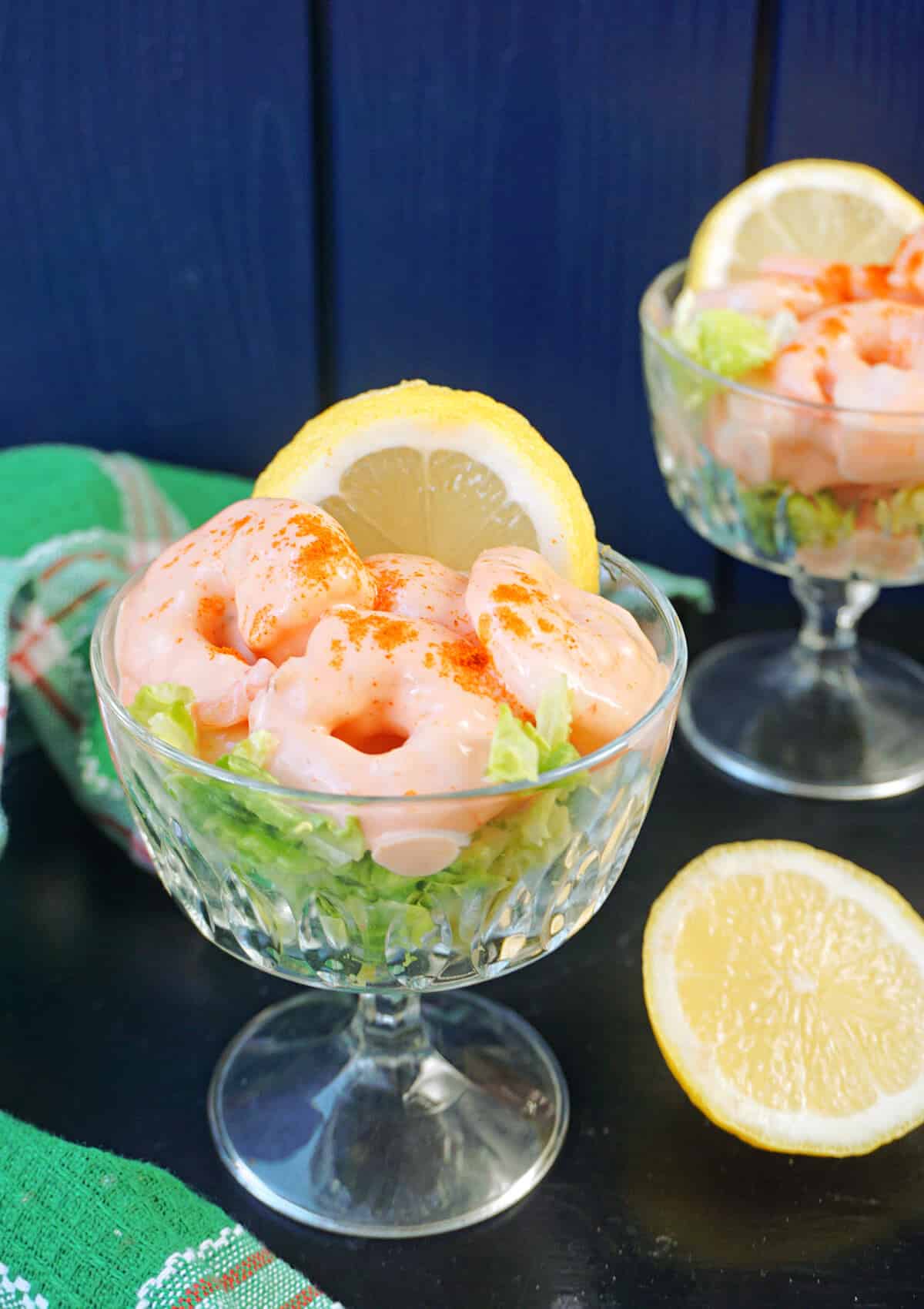 A glass with prawn cocktail, a slice of lemon next to it, and another glass in the background.