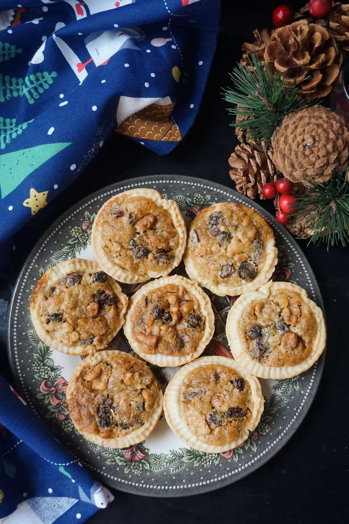A plate with 7 mini tarts with Christmas decorations around.