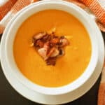 A white bowl with pumpkin and red lentil soup garnished with bacon