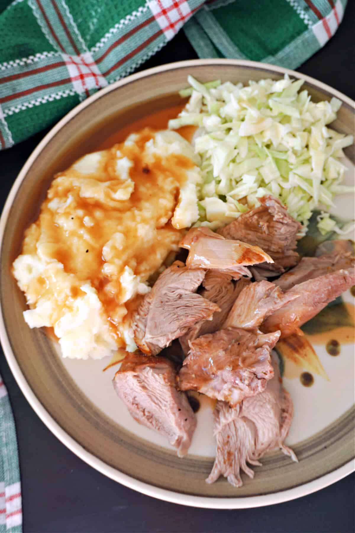 A plate with chopped turkey pieces, mash, gravy and cabbage slaw.