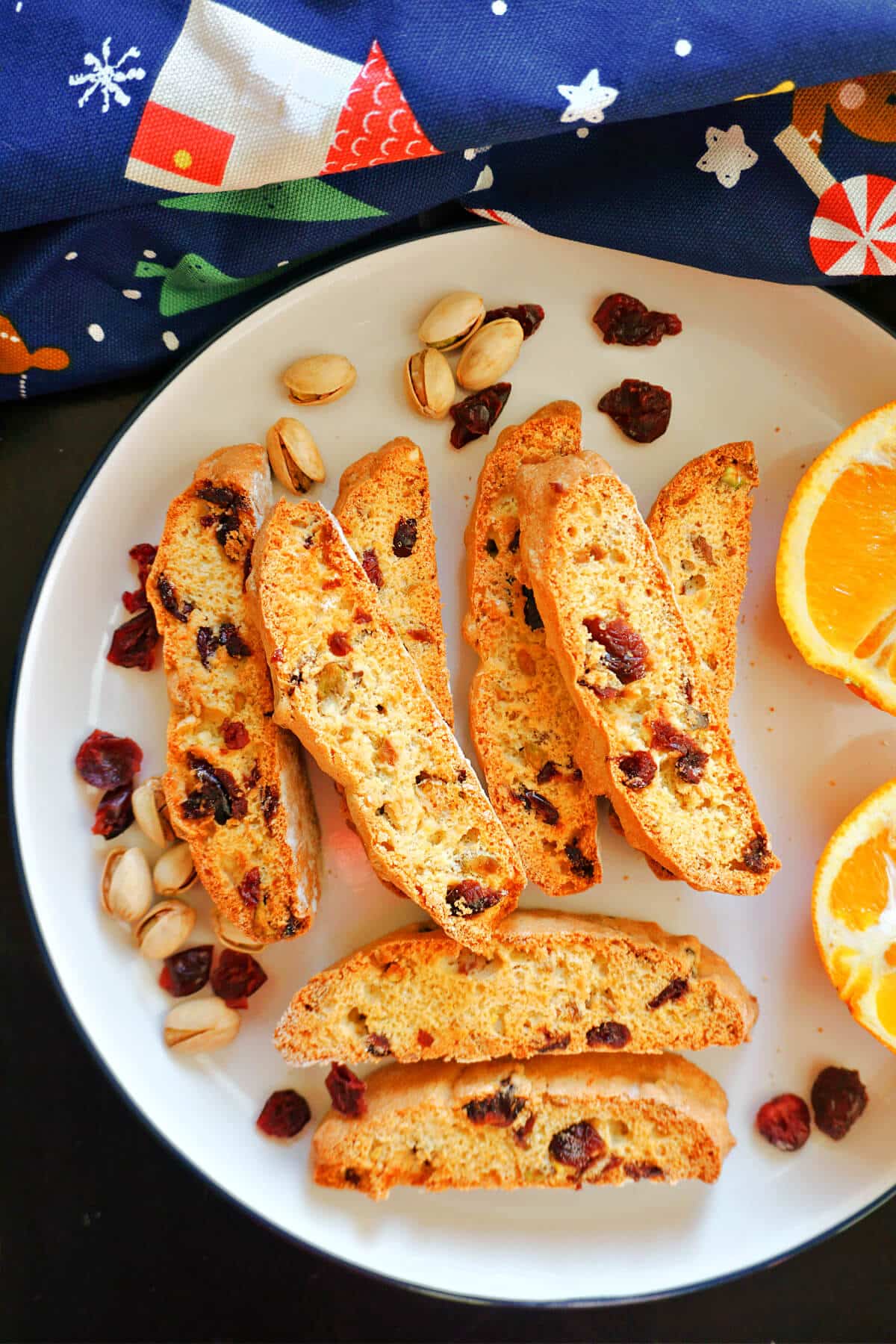 A plate with 8 biscotti with dried cranberries and pistachios around them.