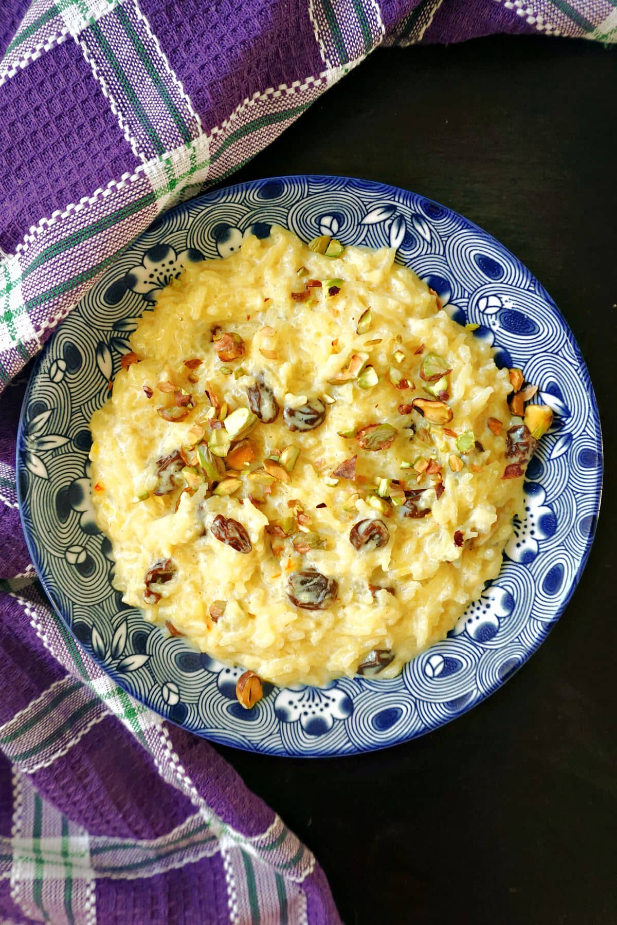 A blue plate with rice pudding topped with chopped pistachios and raisins.