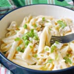 A white bowl with creamy pasta and turkey with peas.