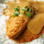 2 Quorn fillet burgers on a bed of rice with katsu sauce over them and garnished with chopped spring onions.