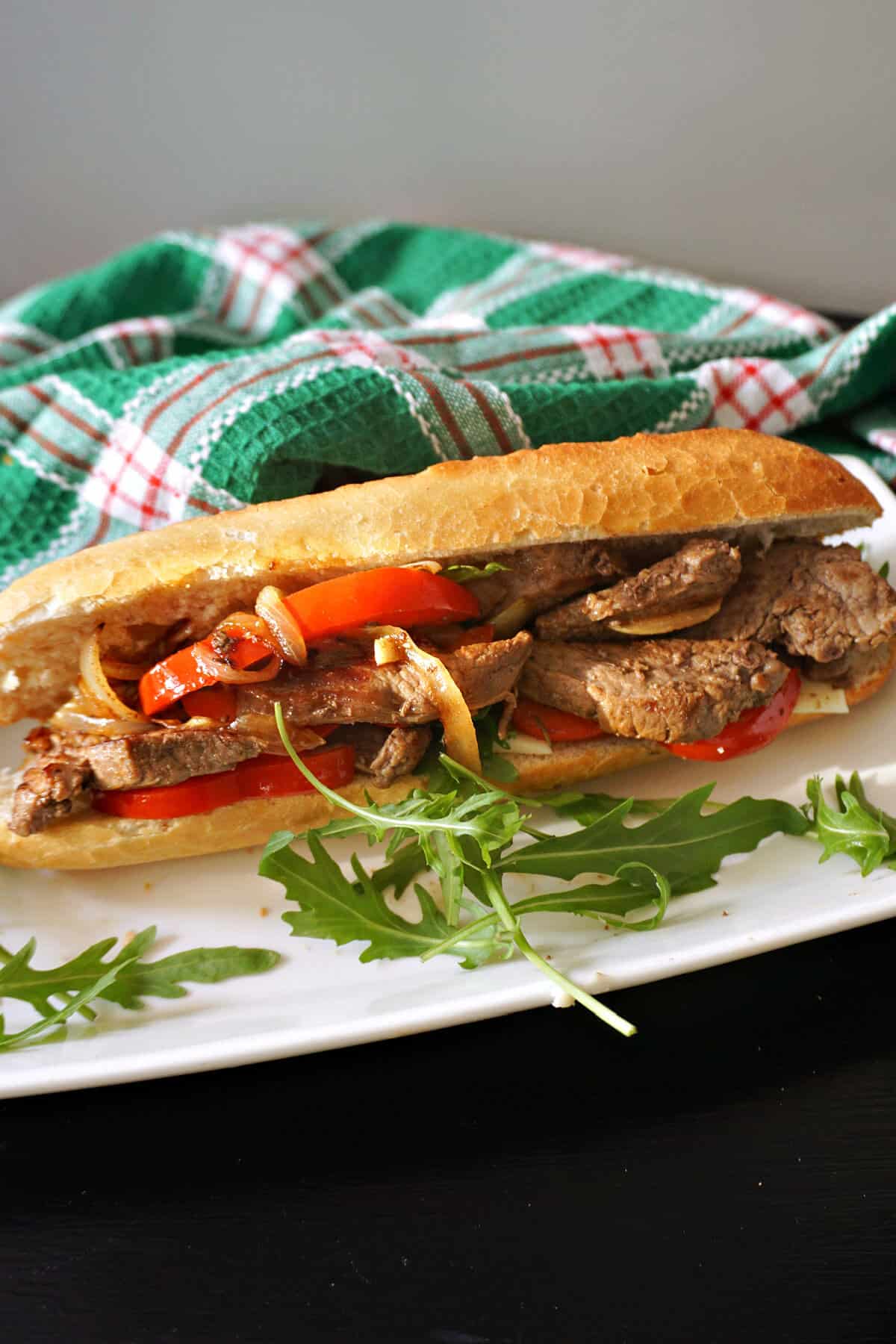 A steak and onion sandwich on a white plate with rocket salad around it.