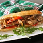 A sandwich with steak and onion on a white plate with arugula salad around it.