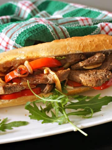 A sandwich with steak and onion on a white plate with arugula salad around it.