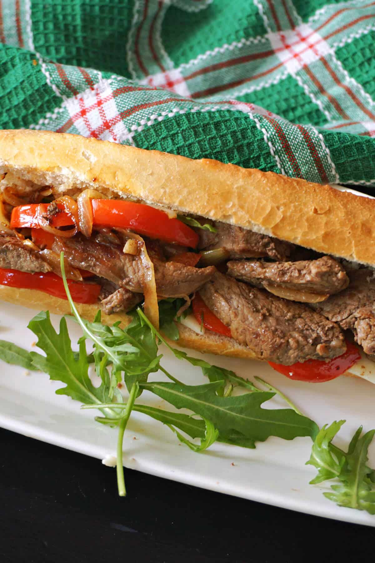 A steak sandwich on a white plate with rocket salad around.