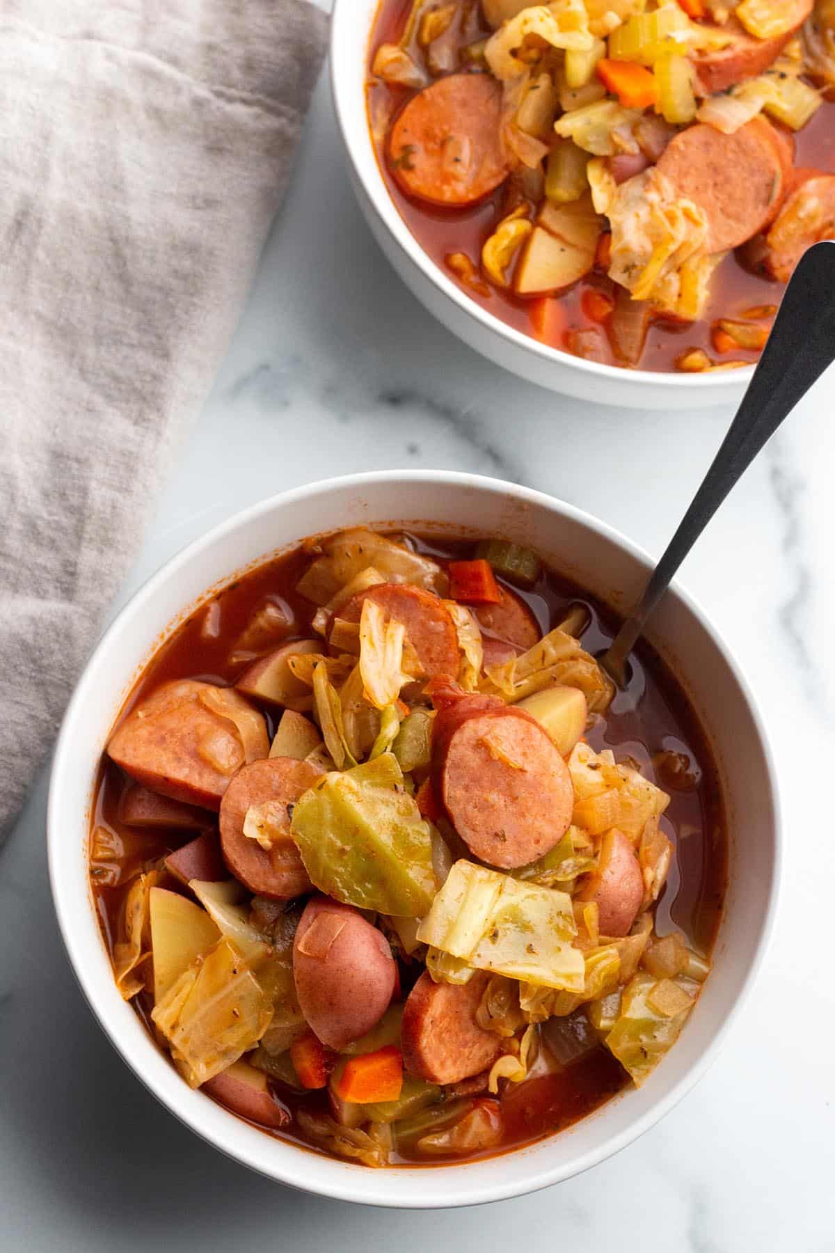 A white bowl with cabbage and sausage soup.