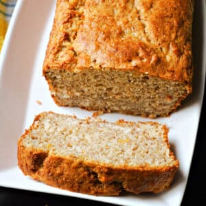 A slice of plantain cake on a white plate with the rest of the bread on it.