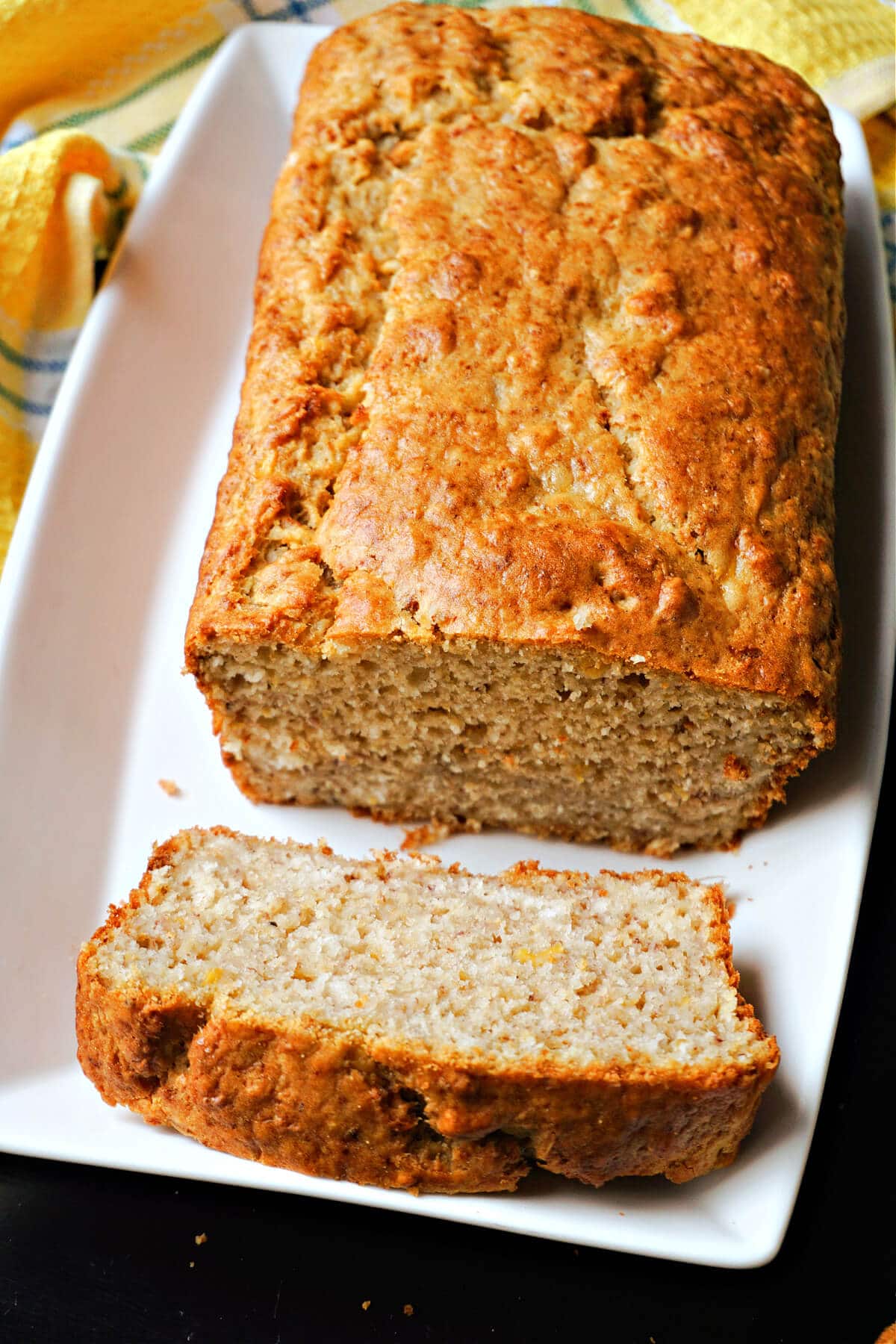 A slice of plantain bread with the rest of the bread on a white rectangle plate.