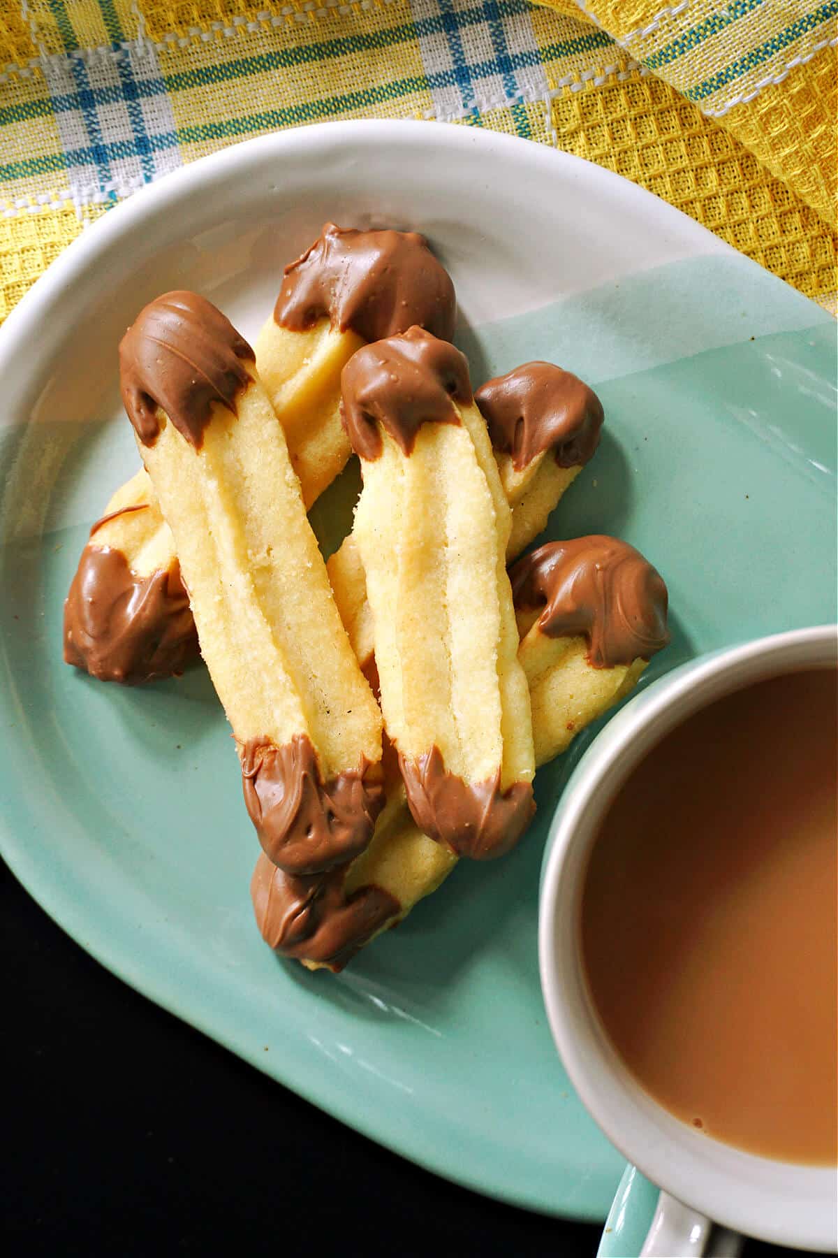 A light blue plate with a cup of tea and 5 Viennese fingers.