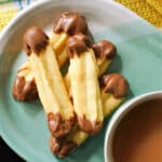 A light blue plate with a cup of tea a 5 Viennese finger biscuits dipped in chocolate.