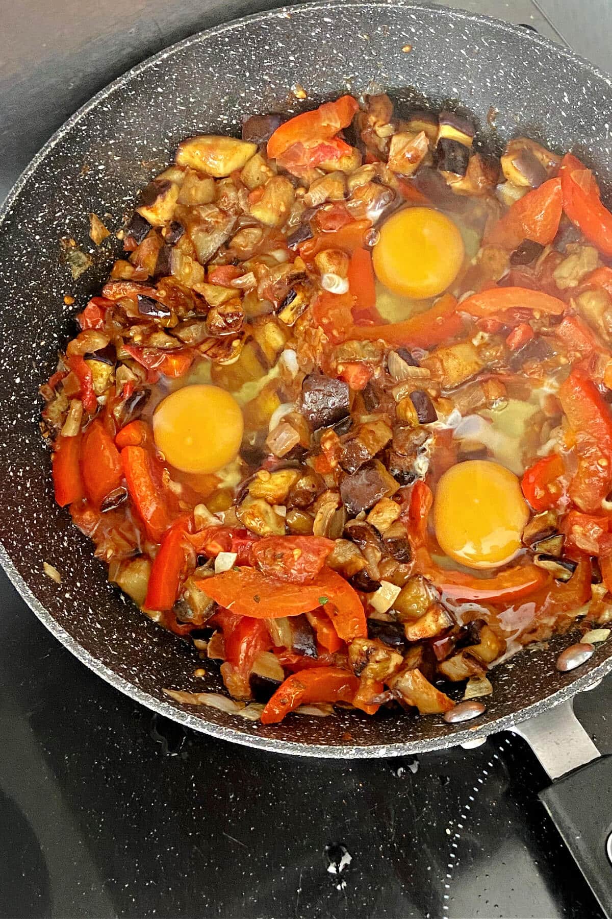 A pan with shakshuka and 3 raw eggs.