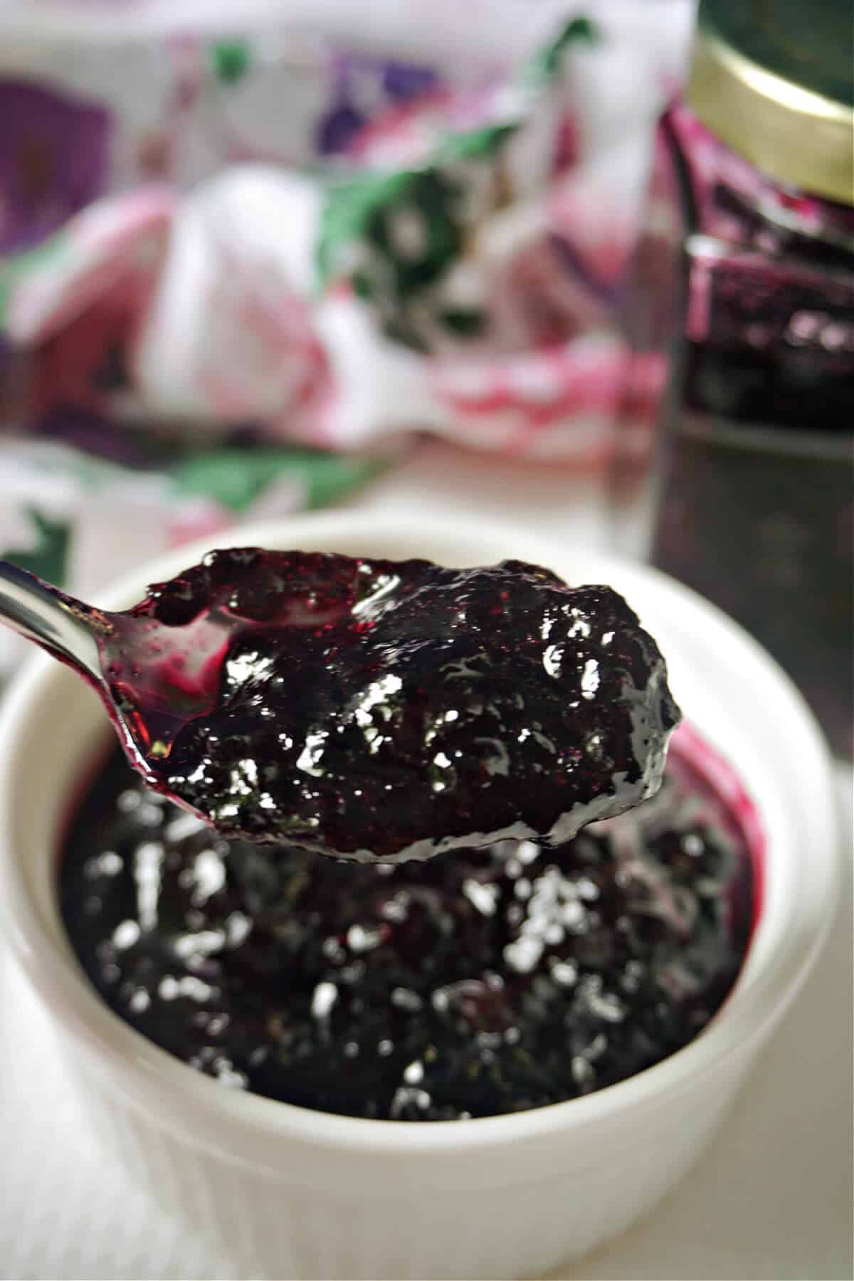 A spoonful of blueberry jam over a white ramekin of more jam.