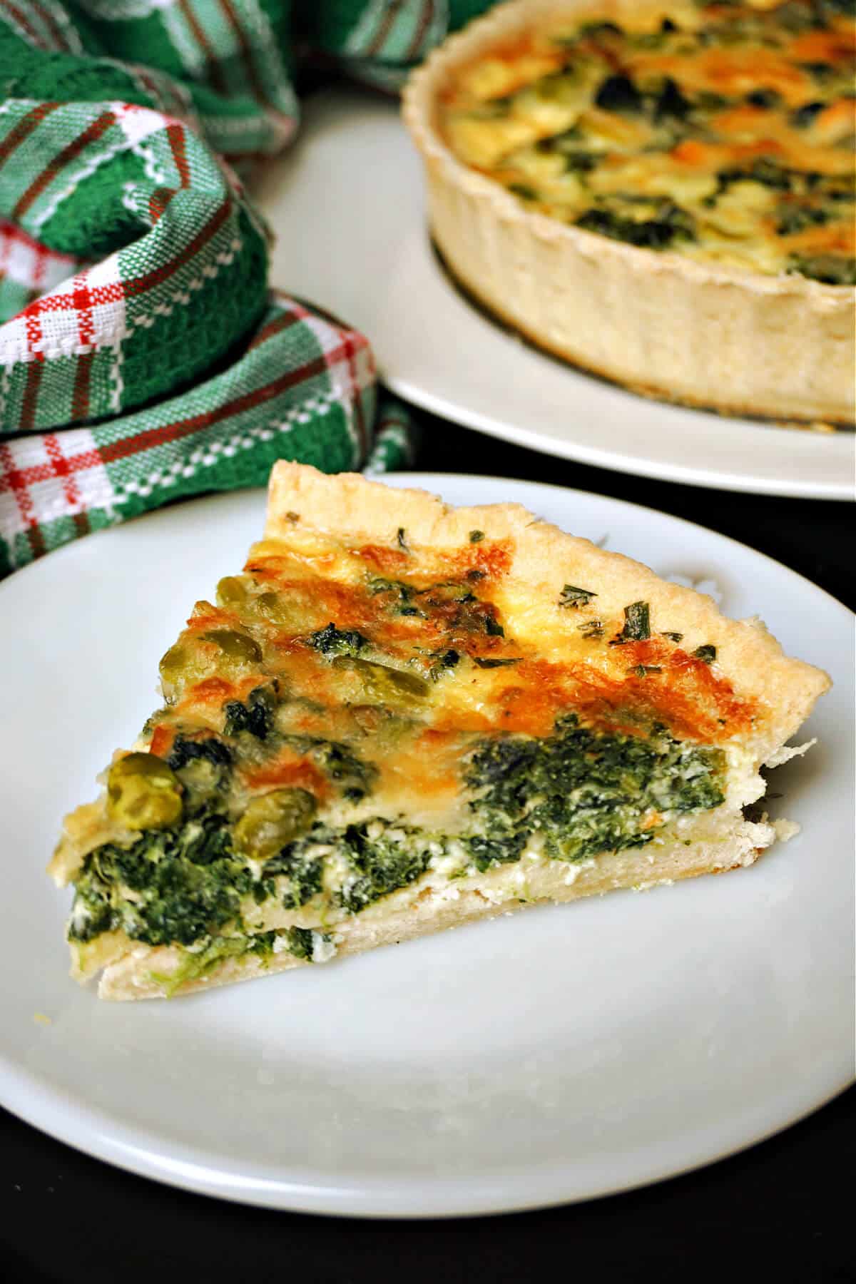 A slice of Coronation quiche on a white plate with the rest of the quiche in the background.