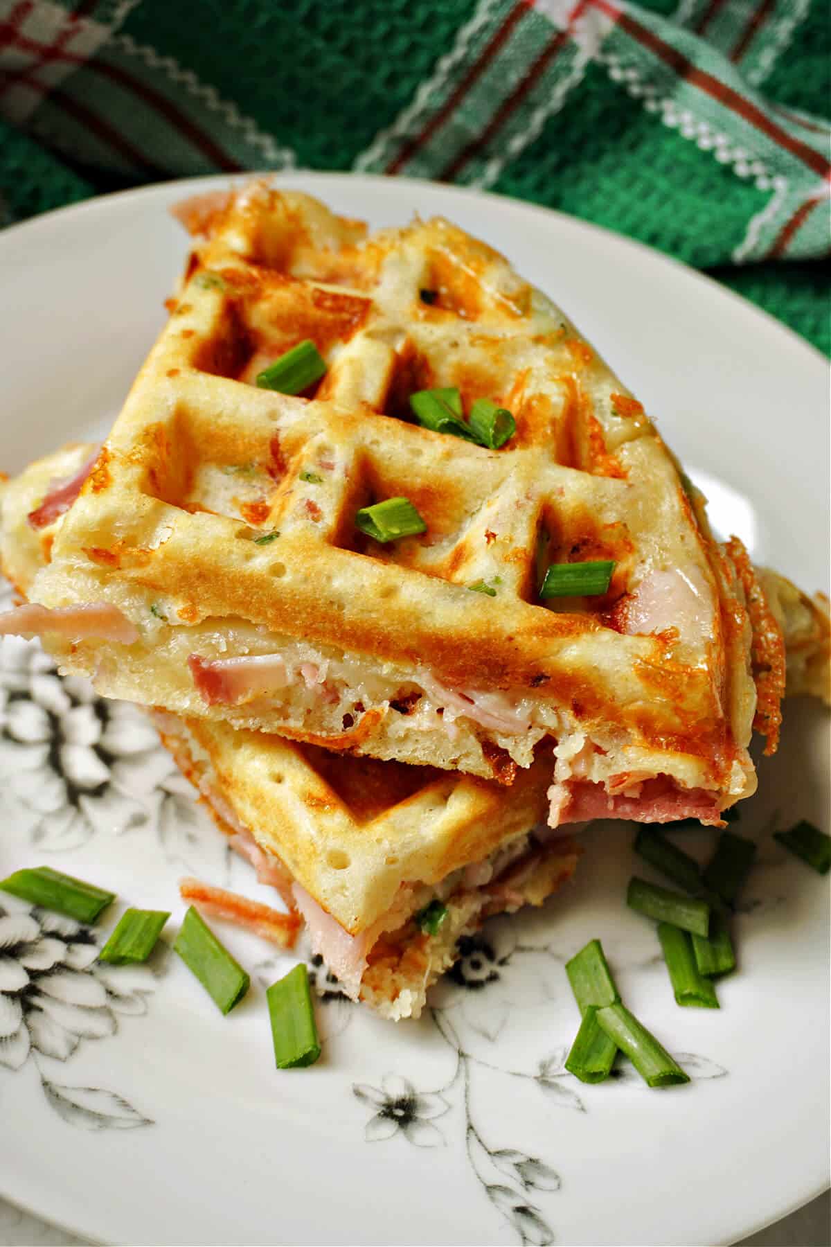 A stack of 2 waffles garnished with chopped spring onions on a plate.