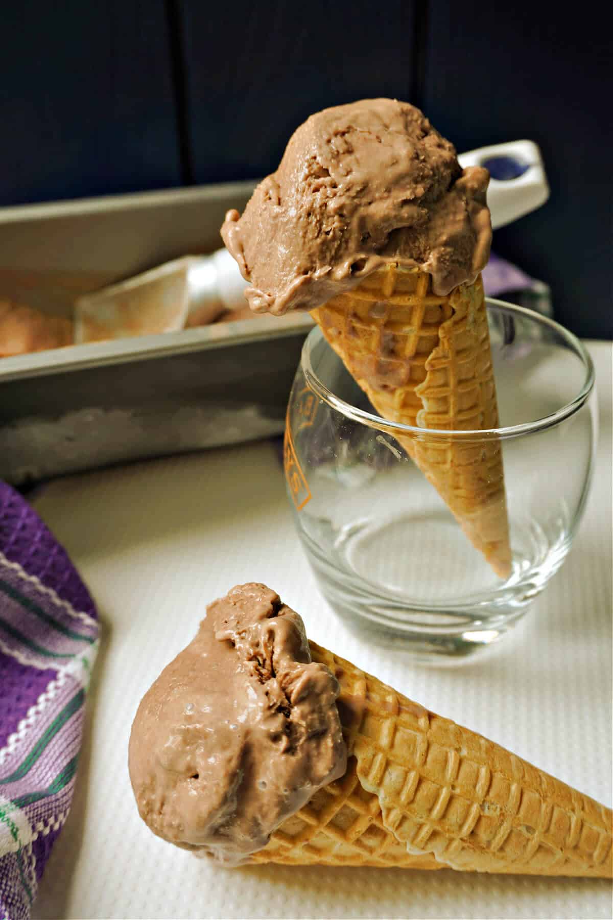 A cone of nutella ice cream in a glass and another cone on a white table.