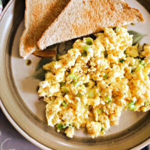 A plate with scrambled eggs and halves of a toast.