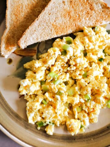 A plate with scrambled eggs and halves of a toast.