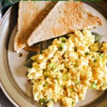 A plate with scrambled eggs and 2 halves of a toast.