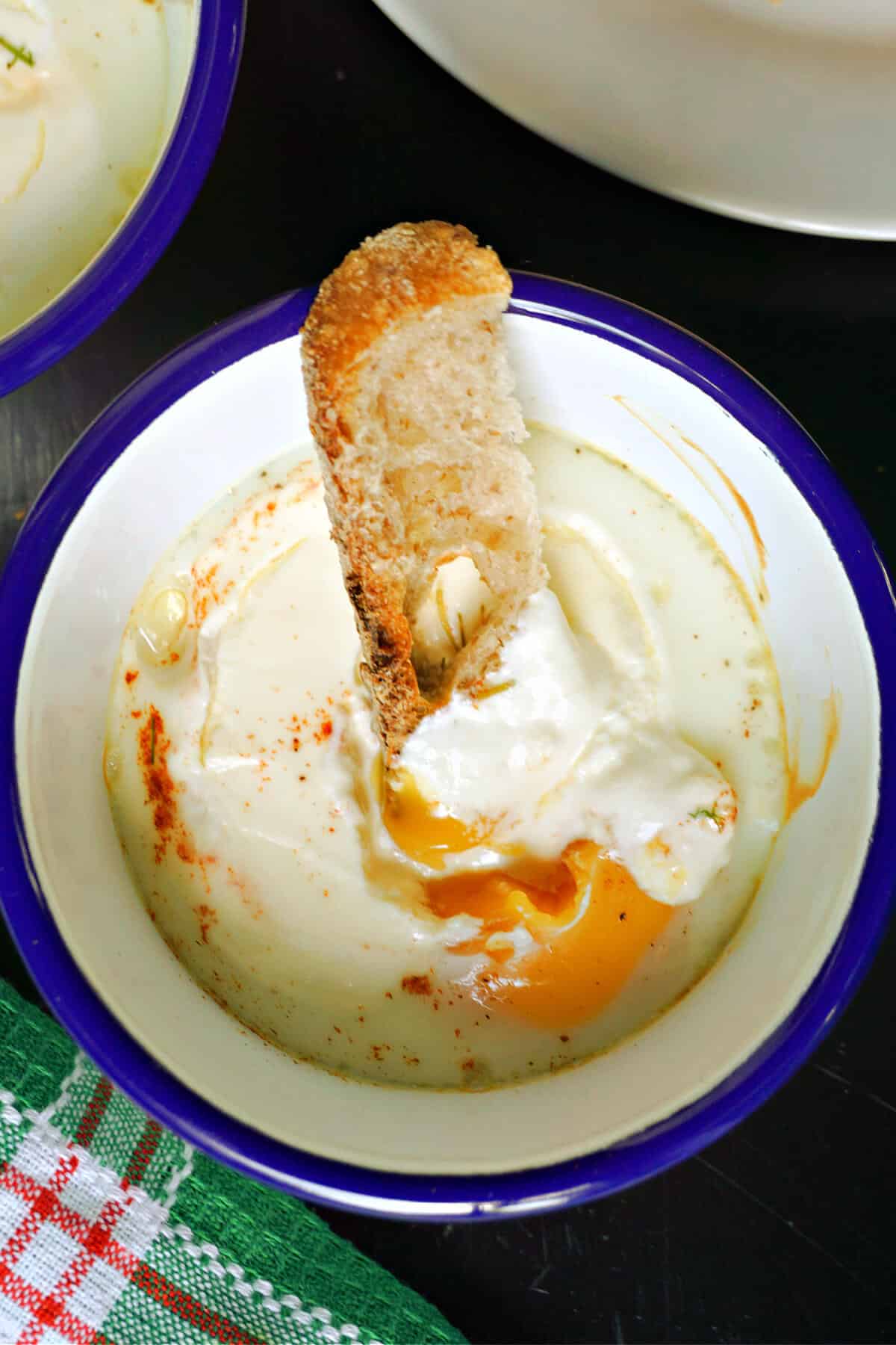 A white and blue ramekin with baked eggs and a bread strip dipped into it.