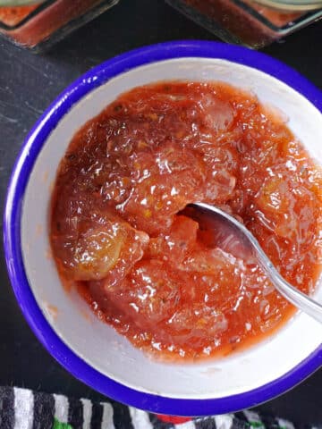 A white ramekin with gooseberry jam and a teaspoon in it.