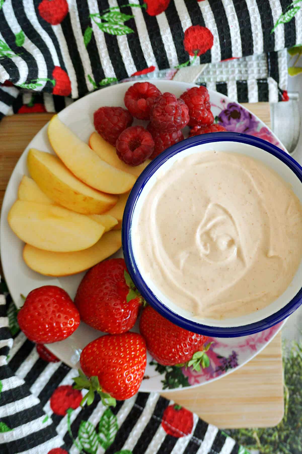 A plate with a small bowl of peanut butter dip and fruit around it.