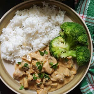 A plate with a portion of cooked basmati rice, pork stroganoff and 4 broccoli florets.