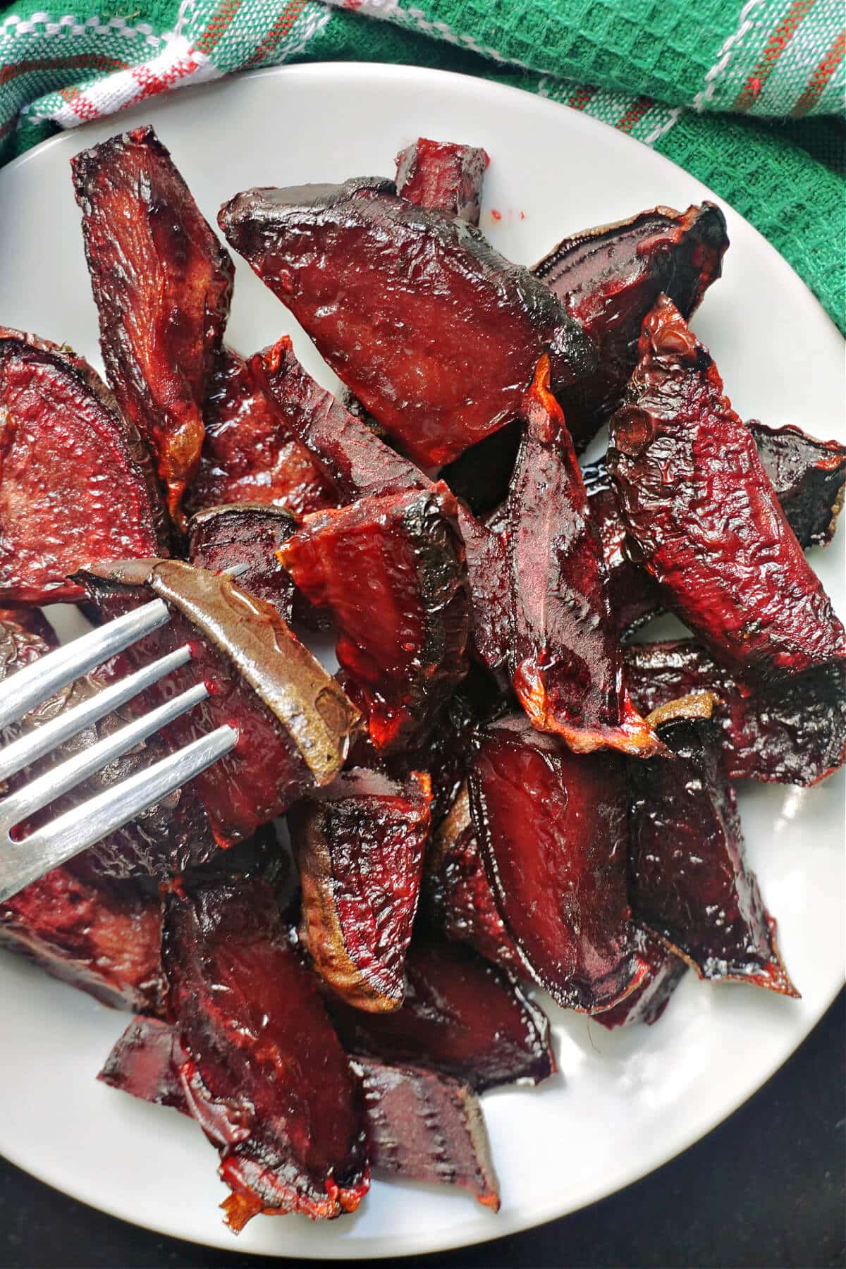 A white plate with roasted beetroot wedges with a fork in.