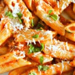 Close-up shoot of a pasta dish in a roasted tomato and red pepper sauce garnish with parmesan and basil.