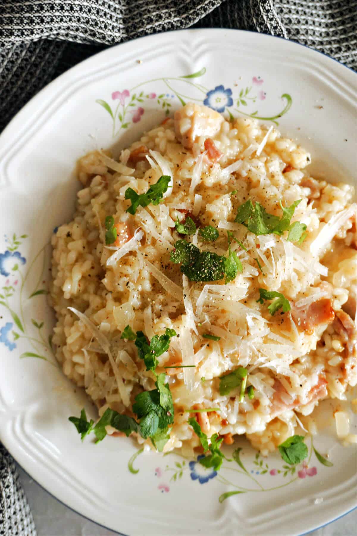 A white plate with bacon risotto topped with parmesan and parlsey.