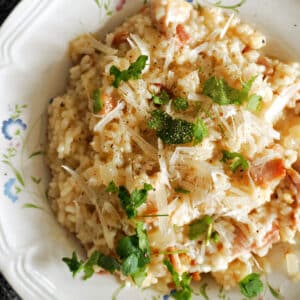 A white plate with bacon risotto garnished with parsley and parmesan.