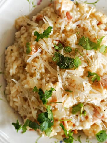 A white plate with bacon risotto garnished with parsley and parmesan.