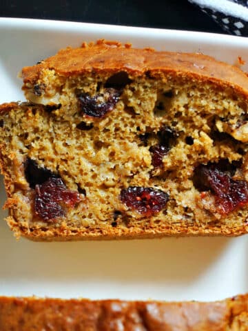 A slice of banana pumpkin bread with cranberries and walnuts on a white plate.