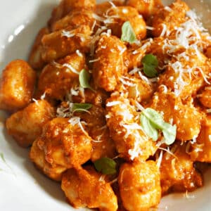 A white plate with a portion of gnocchi in tomato sauce and garnished with parmesan cheese.