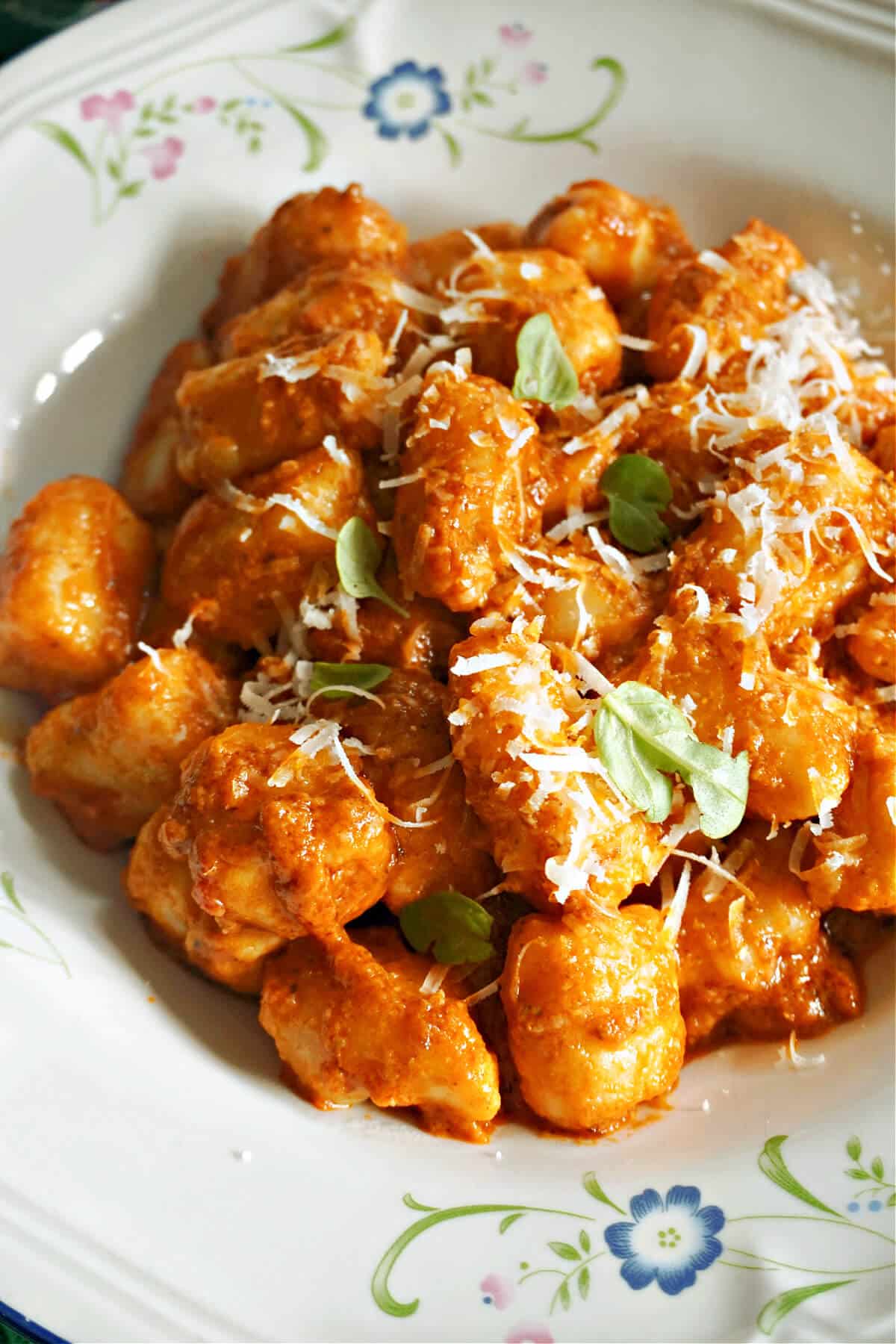 A white plate with gnocchi in tomato sauce.