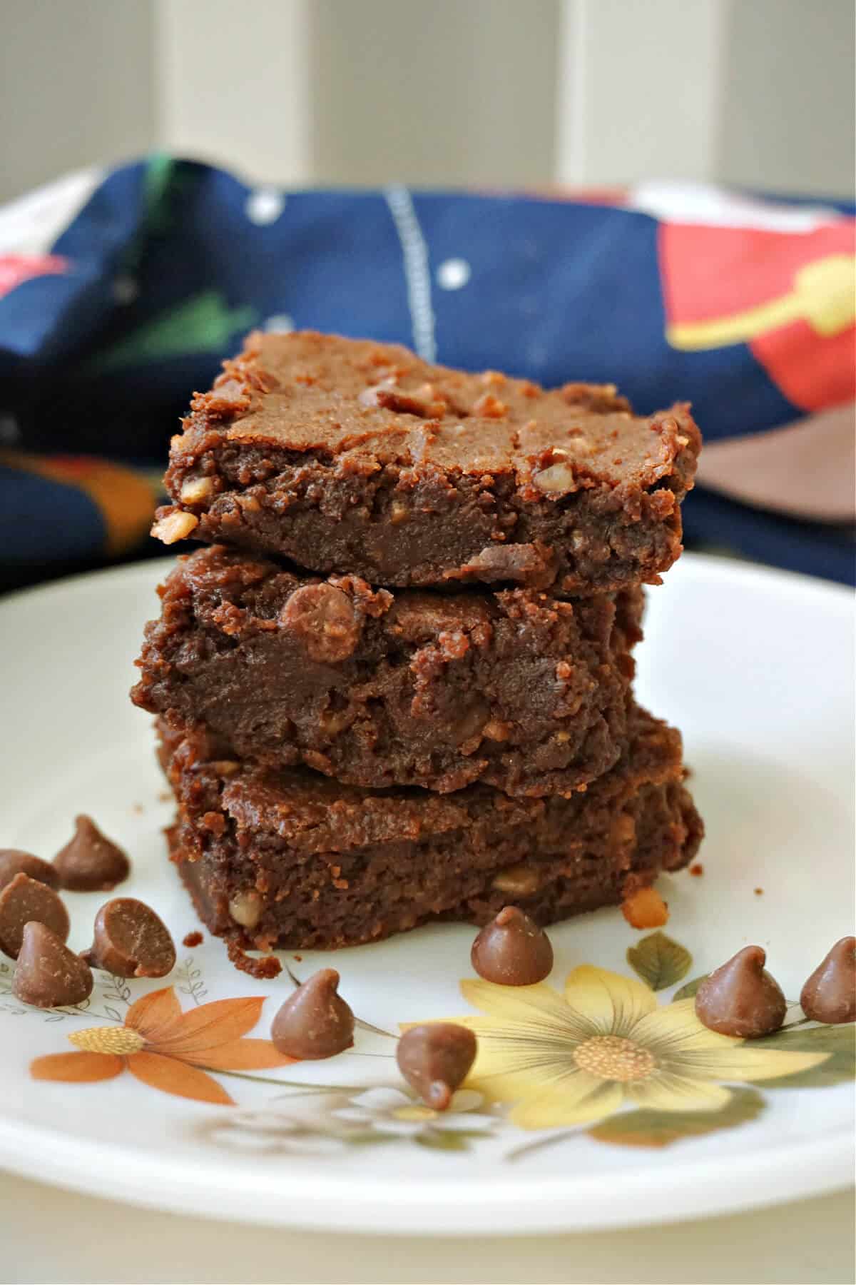 A stack of 3 brownies on a plate with chocolate chips.