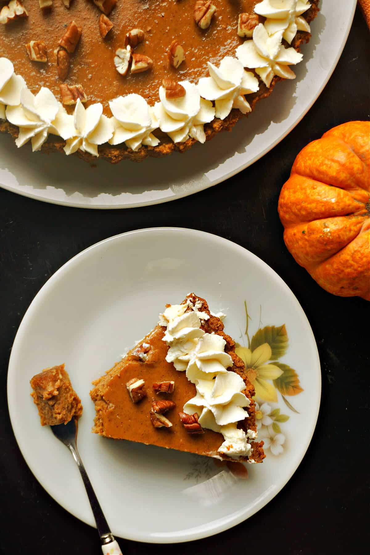 Overhead shoot of a small plate with a slice of pumpkin pie and more pie on a larger plate.