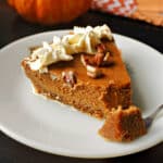 A slice of pecan crust pumpkin pie on a white plate with a forkful of pie.