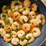 A frying pan with prawns in sauce garnished with parsley.
