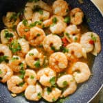 A frying pan with prawns cooked in sauce and garnished with parsley.