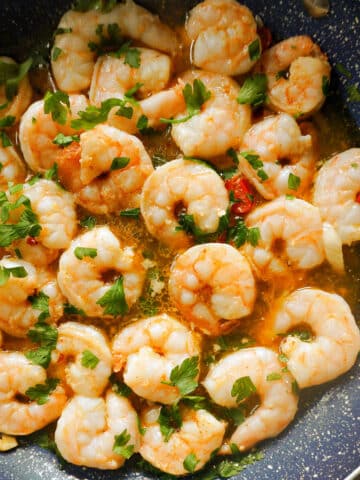A frying pan with prawns cooked in sauce and garnished with parsley.