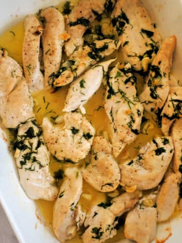 A white dish with chicken tenders cooked in a butter sauce with herbs and garlic.