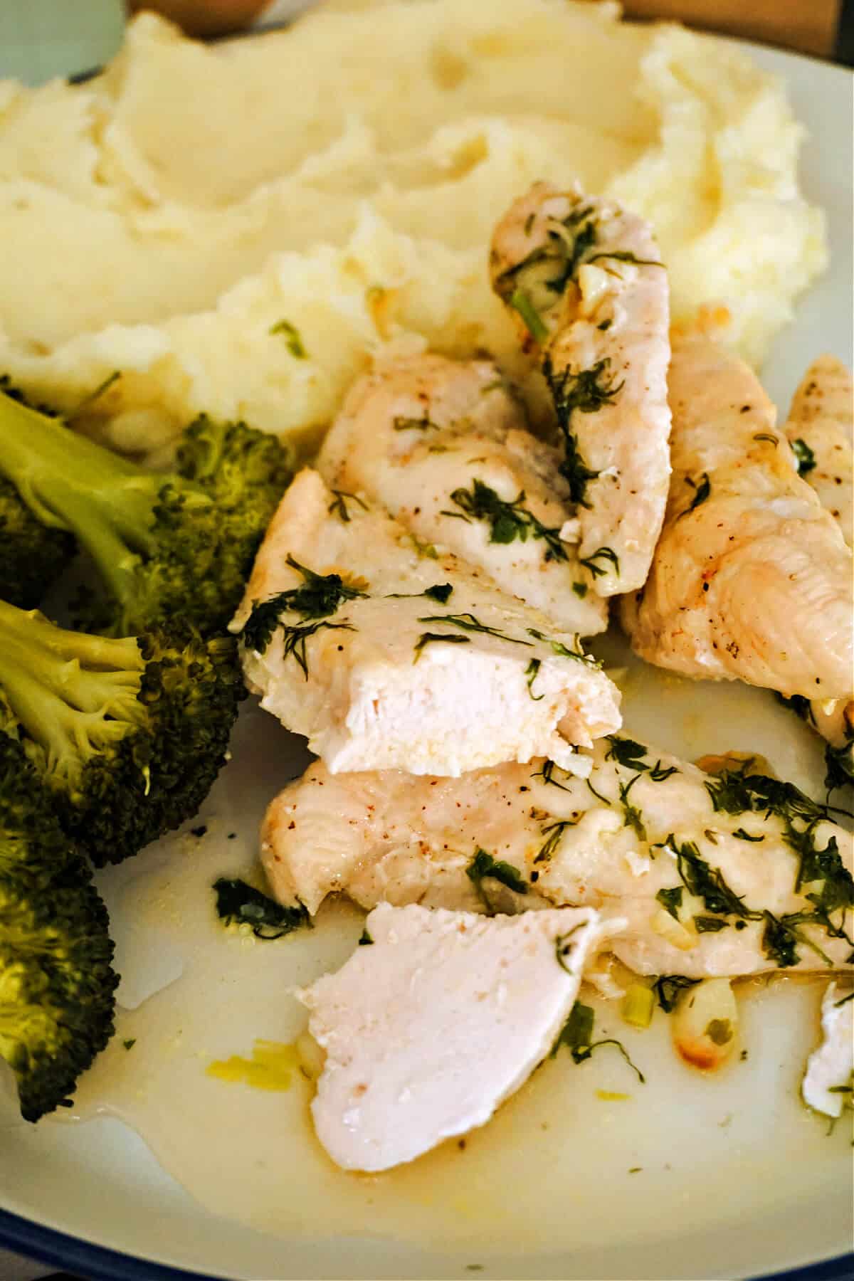 Chicken tenders with mash and broccoli florets on a white plate.