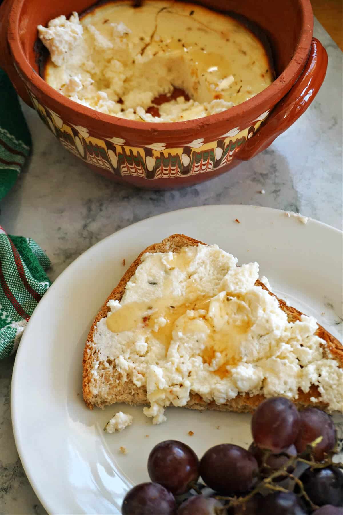 A white plate with half of a slice of toast with ricotta spread and a dish with more spread.